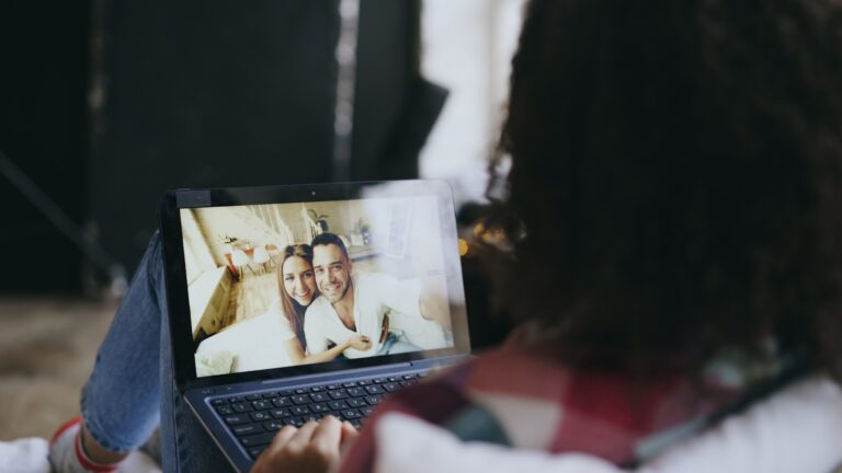 Woman video calls couple on laptop outdoors.